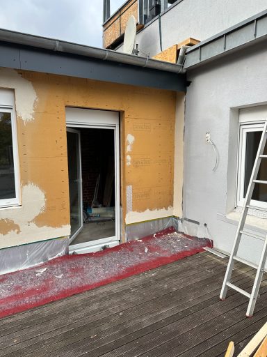 Bauarbeiten an einer Terrasse mit unvollständiger Fassadenverkleidung und einer Leiter.