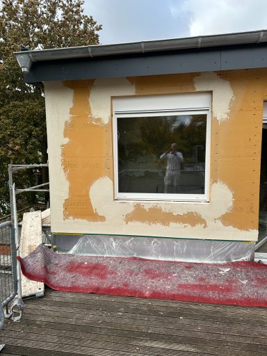 Fassade eines Hauses mit unvollständigem Putz und einem Gerüst im Vordergrund.