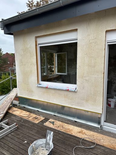 Renovierung eines Hauses mit offenem Fenster und Baustellenmaterialien auf der Terrasse.